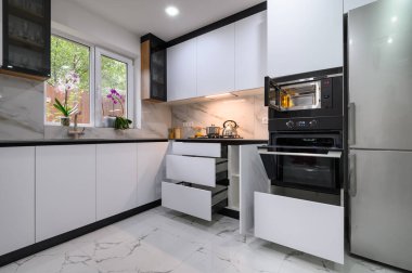 A contemporary kitchen with white cabinets, a marble floor, an open oven door, and pull-out shelves for easy access to ingredients and appliances.