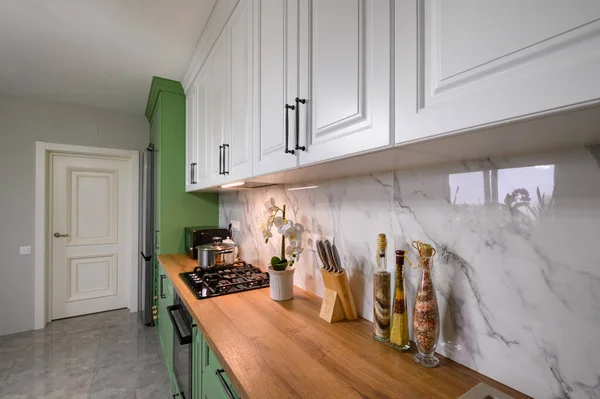 Green and white colored modern kitchen details, closeup to wooden counter