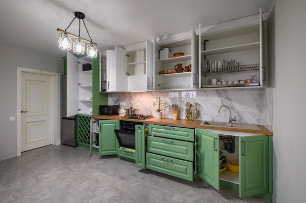 Doors open and drawers pulled out at new green and white kitchen furniture, showcase interior