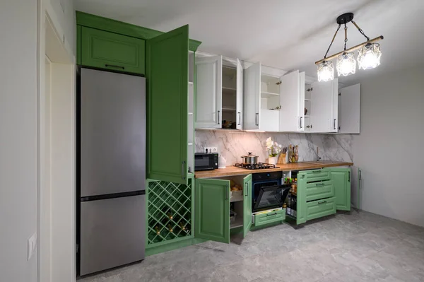 Doors open and drawers pulled out at new green and white kitchen furniture, showcase interior