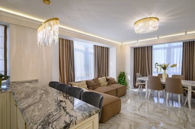 A cozy brown sofa and pillows in a studio apartment with a classic kitchen and living room featuring a spacious and brightly lit design in creamy color