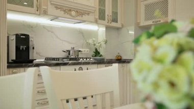 Slider track shot of large luxury trendy beige moden classic kitchen, white dining table with bunch of flowers on it
