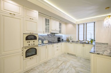 Krem renkli klasik mutfak ve stüdyo dairesinin içinde yemek alanı olarak kullanılan ada, yastıklı ve perdeli rahat kahverengi kanepe