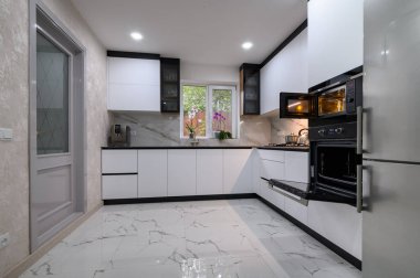 A renovated kitchen with a white, minimalist design and a beautiful marble floor. The open oven door adds a touch of warmth and coziness.