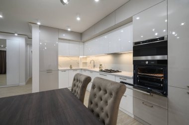 Duvarında televizyon olan büyük, beyaz, lüks bir stüdyo dairenin içinde büyük bir mutfak, bir sürü fotokopi alanı, sandalyeli yemek masasının yakın görüntüsü.