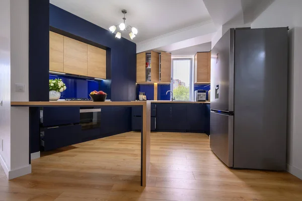 Luxury large blue and wood colored kitchen in studio apartmentafter good renovation, closeup to counter, some drawers pulled out, unrecognizable person at background