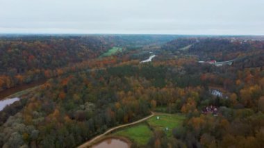 Letonya 'nın Sigulda şehrinde Gauja Nehri yakınlarında sonbahar. Renkli Ormanlar ve Vadi İHA 'sı Gauja Ulusal Parkı' nı vurdu. Şeytan Uçurumu Köprüsü Gauja Nehri üzerinde Kayak Resort Kakitis 'ten görünüyor