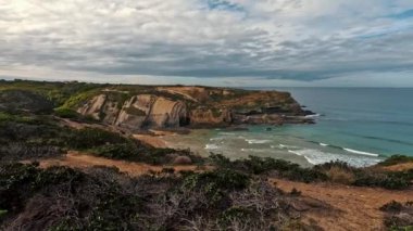 Zambujeira deniz kıyısında deniz dalgaları, uçurumlar ve kumullarla kaplı yeşil bitki örtüsü kırmızı incir yaprakları, güneşli bir gün, açık mavi gökyüzü. Rota Vicentina Sahili, Portekiz.