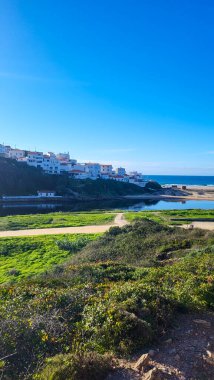 Praia De Ohexe Mar Sahili Altın Kum, Atlantik Okyanusu, Nehir Bükme ve Aldatma Köyü 'nün Beyaz Evleri ile. Rota Vicentina Sahili, Odemira, Portekiz. Rota Vicentina 'nın Balıkçı Patikası' nda yürüyüş.