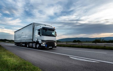 Big White truck driving on the highway through countryside landscape at sunset. clipart