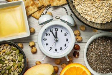 Diyet zamanı. Yemek saati. Yulaf gevreği, fındık, chia tohumu, kabak çekirdeği, ayçekirdeği, bal, çavdar ekmeği ve beyaz ahşap zemin üzerinde bir çalar saat ile sağlıklı beslenme