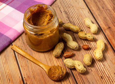 Masada kremalı fıstık ezmeli kavanoz ve tahta kaşık ve masaya saçılmış kabuklu fıstıklar.