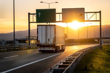 Günbatımı şehir manzaralı, hızlı teslimat, kargo lojistik ve nakliye konsepti olan büyük bir teslimat kamyonu yolda ilerliyor.