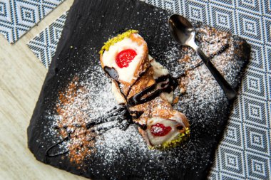 İtalyan Sicilyalı cannolo tatlısı siyah taş tabak makrosu üzerine yakın plan sarı kabuklu ve ricotta peynirli ve şamfıstıklı krema ile cannoli dilimli.