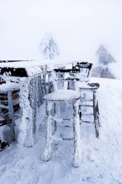 Dağlarda kış manzarası. Karla kaplı ve donmuş kır evi ve açık hava masaları ve bir restoranın sandalyeleri. Dağ vadisinde buzlu açık hava manzarası. Doğa konseptinin güzelliği.