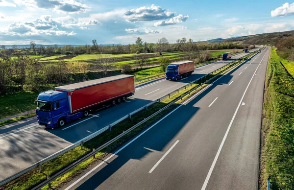 美しい青空の下の田舎の高速道路に赤いトレーラーを並べた青い輸送トラックのコヨーテと高速輸送シーン ストック画像