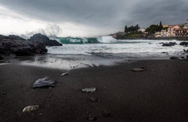Yağmurlu ve bulutlu bir günde dalgalar kıyıya vuruyor. Kiklops Sahili, siyah volkanik kayalar ve Sicilya 'ya, Acireale kasabasının yakınlarına gönder.