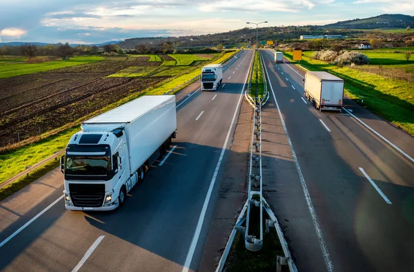 美しい青空の下の田舎の高速道路の反対の方法を通る白い輸送トラックのコンヴェイスと高速道路上の重い交通シーン ストック写真