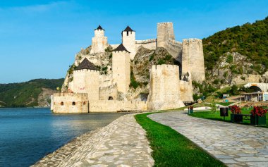 Ortaçağ Golubac kalesi, Tuna 'nın sularını yansıtıyor. Sıcak günbatımı ışığıyla aydınlanan kale kuleleri, mavi gökyüzü. Hava görüntüsü. Sırbistan 'ın ünlü turizm merkezi.