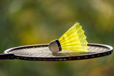 Açık hava badminton sahasında yeşil arka planda doğal ışık gölgesi olan parlak sarı badminton mekik ve raket, bulanık badminton arka plan, kopyalama alanı.