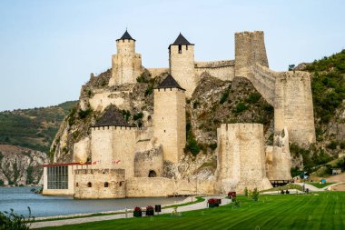 Ortaçağ Golubac kalesi, Tuna 'nın sularını yansıtıyor. Sıcak günbatımı ışığıyla aydınlanan kale kuleleri, mavi gökyüzü. Hava görüntüsü. Sırbistan 'ın ünlü turizm merkezi.