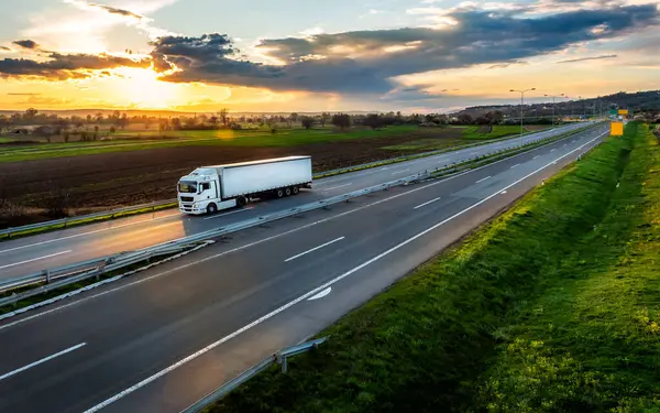 日没の田舎の風景でアスファルトハイウェイ道路のトレーラー付きの白い輸送トラック ストック写真