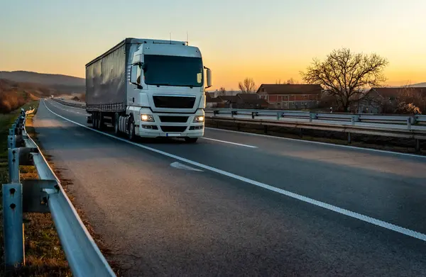 Büyük beyaz bir kamyon gün batımında ormanlık araziden geçiyor..