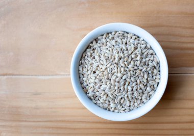 Bir kase arpa taneciği, ahşap bir masa arkasında izole edilmiş.