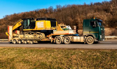 Otoyol boyunca inşaat makinesi kazıcısı, Backhoe taşıyan nakliye ya da çekici.