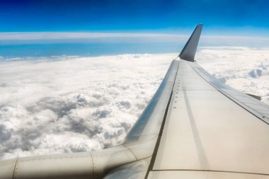 Bulutların üstünde bir uçağın kanadı. Uçak penceresinden bulutlara ve günbatımına kadar olan manzara. Kalın beyaz bulutların üzerinde uçak kanadı.
