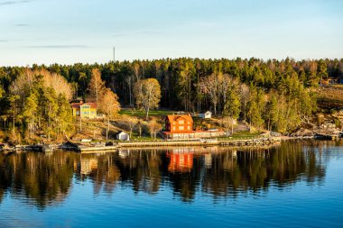 Baltık Denizi 'ndeki Stockholm takımadalarında bir köprüye bağlı küçük bir ada. Güneşli bahar akşamları geleneksel beyaz ve kırmızı evle birlikte..