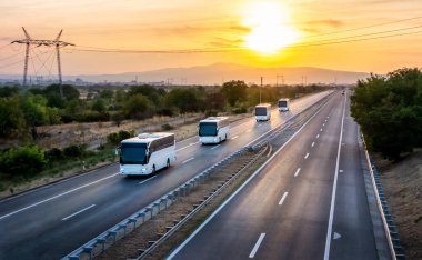 Güzel dramatik bir günbatımı ile geniş bir otoyolda seyahat eden dört modern beyaz otobüsün serisi. Otobüs konvoyu. Yolcuların otobüs hattında karayolu taşımacılığı.