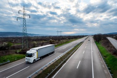 Kırsal bir otoyolda, dramatik bir günbatımı gökyüzünün altında beyaz nakliye kamyonu