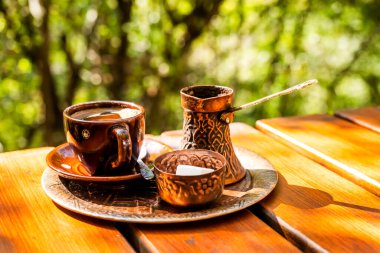 Kahverengi seramik fincanda sade kahve, klasik bakır kahve demliği ve kırsal ahşap masada bir kavanoz şeker küpü.