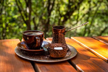 Kahverengi seramik fincanda sade kahve, klasik bakır kahve demliği ve kırsal ahşap masada bir kavanoz şeker küpü.