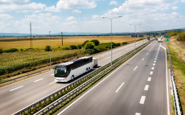 Beyaz, modern, rahat turist otobüsü, güneşli, güneşli bir gün batımında otoyoldan geçiyor. Seyahat ve turizm konsepti. Yolculuk ve yolculuk araçla.