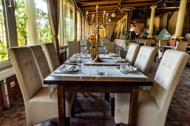 İç mekan modern restoran, servis, ziyafet, dekor, masa örtüsü servis masası, şarap bardakları, tabaklar, geniş pencerenin yanındaki çatal bıçak seti. Kavram masası yemek için hazır.