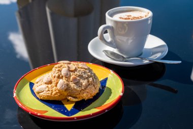 Bir fincan kahveyle birlikte renkli tabakta servis edilen bademli kurabiyeler. Lezzetli bir çift bademli kurabiye, lezzetli ikramlar gevrek dokuları tatlı tatlarla birleştirir, her durum için idealdir.