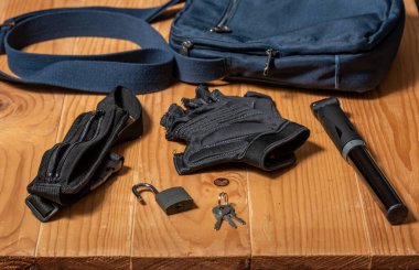 Açık havada ve tahta bir masada bisiklet malzemeleri. Bel bükme, kilit, anahtar, bisiklet eldivenleri, pompa ve omuz çantası.