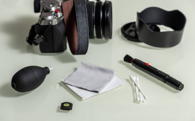 Aynasız kamera ve objektifle kamerayı temizlemek için aletler, flaş. Beyaz cam masadaki farklı nesneler