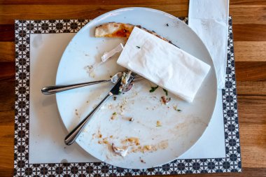 Tahta bir masada pizza yedikten sonra yemek artıklarıyla dolu boş bir tabak.