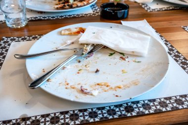 Tahta bir masada pizza yedikten sonra yemek artıklarıyla dolu boş bir tabak.