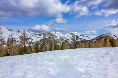 Mavi bulutlu gökyüzünün altındaki karla kaplı dağların manzarası