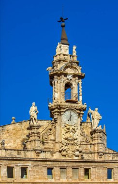 Süslü saat kulesi, azizlerin ve meleklerin heykelleri ve Valencia 'daki parlak mavi gökyüzü altında zengin dekoratif taş işleriyle barok tarzı kilise cephesi.