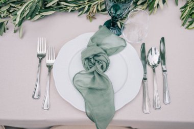 Çatal bıçak, peçete, zeytin dalları ve tabak manzaralı şık bir ortam.. 