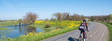 Hollanda, Hollanda, 19 Nisan 2023: Hollanda 'da nehir vadisi ve bisiklet su baskını kanalı üzerinde mavi bahar gökyüzü altında, Beytül' de tiel yakınlarında sarı çiçekler