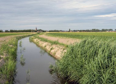 Belçika 'nın Batı Flanders bölgesindeki kanal ve tarlaların arkasındaki kilise ve köy.