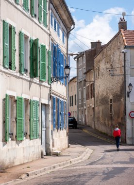 Elektrikli scooterlı çocuk, küçük bir Fransız kasabasında yeşil ve mavi panjurlu eski cephelerden geçer.