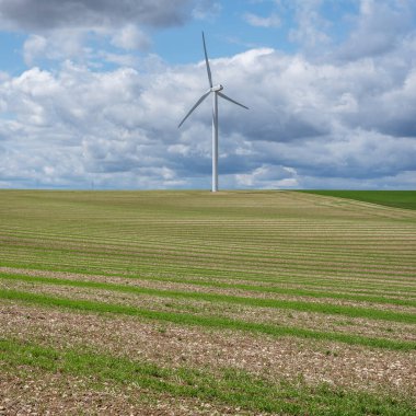 Kuzey Fransa 'nın kırsal kesimlerinde rüzgâr türbinleri olan neredeyse soyut tarlalar üzerinde bulutlu bir gökyüzü.