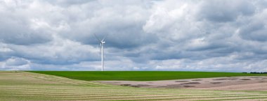 Kuzey Fransa 'nın kırsal kesimlerinde rüzgâr türbini olan neredeyse soyut tarlalar üzerinde bulutlu bir gökyüzü.